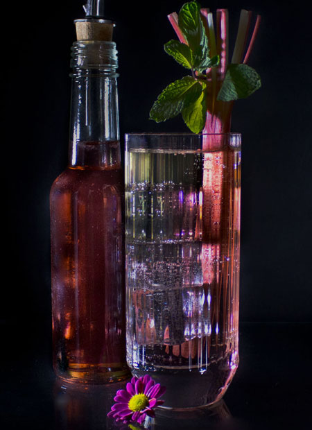 Roter Sirup in einer Flasche und Longdrinkglas mit Rhabarber-Stengel.