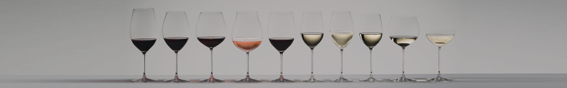 Zahlreiche Weingläser und andere Stielgläser aus der Serie Riedel Veritas stehen gefüllt nebeneinander.