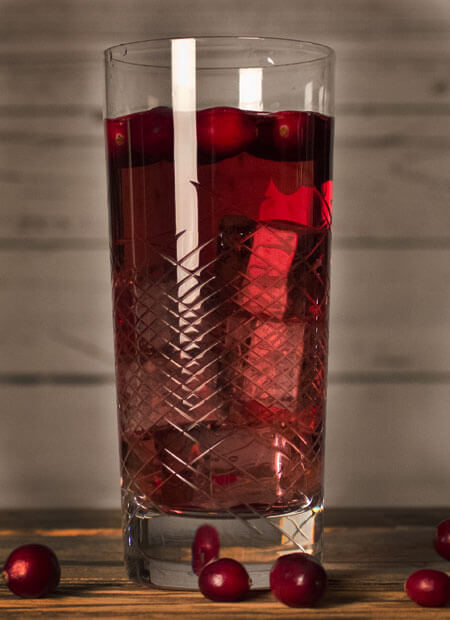 Hohes Longdrinkglas gefüllt mit einem dunkelroten Drink und Eiswürfeln.