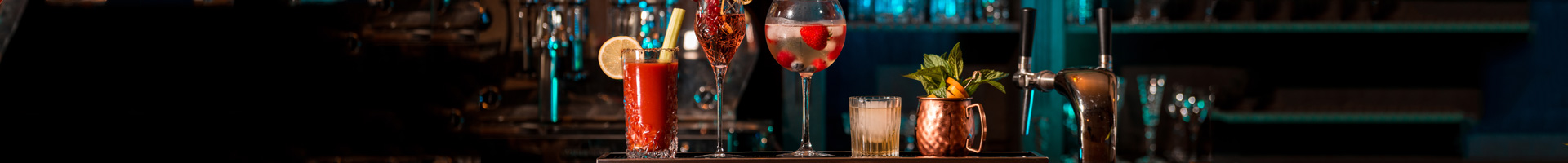 Cocktailgläser von Barstuff mit farbenfrohen Cocktail-Kreationen stehen auf dem Tresen in einer Reihe.