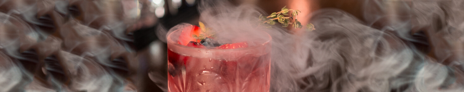 Ein Glas mit rotem Drink umgeben von hellen Rauchschwaden.