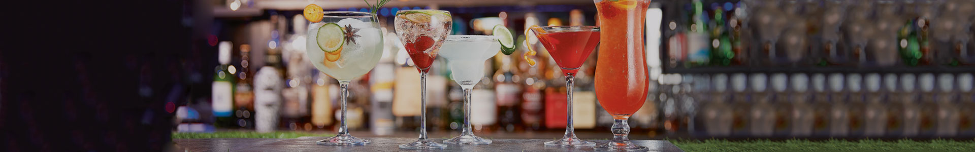 Unterschiedliche Cocktailgläser von Chef & Sommelier stehen nebeneinander auf einen Bar-Tresen und sind mit bunten Cocktails gefüllt.