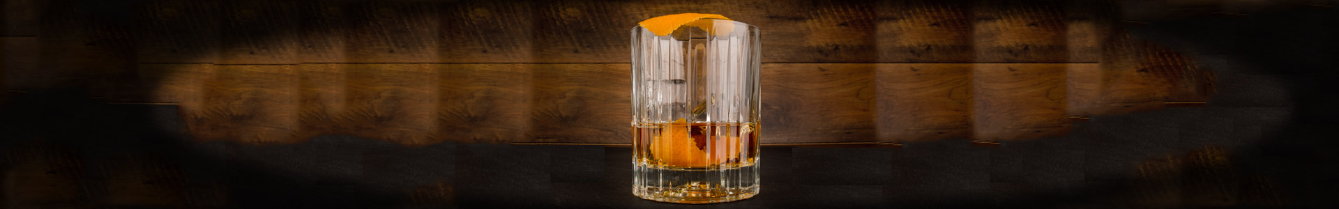 Tumbler Glas mit Whisky und Orangenzesten.