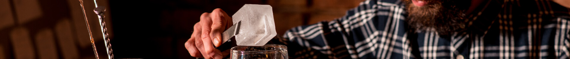 Ein Barkeeper hält mit einer Eiszange einen großen Eiswürfel fest.